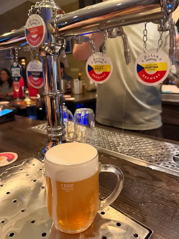 A glass mug of pale lager on the bar under chrome taps labelled with Bohem Brewery's Sparta, Amos and Martina lagers.